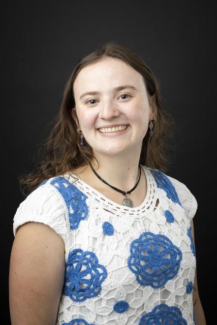 Professional headshot of person in white blouse with blue flowers against a black backdrop.